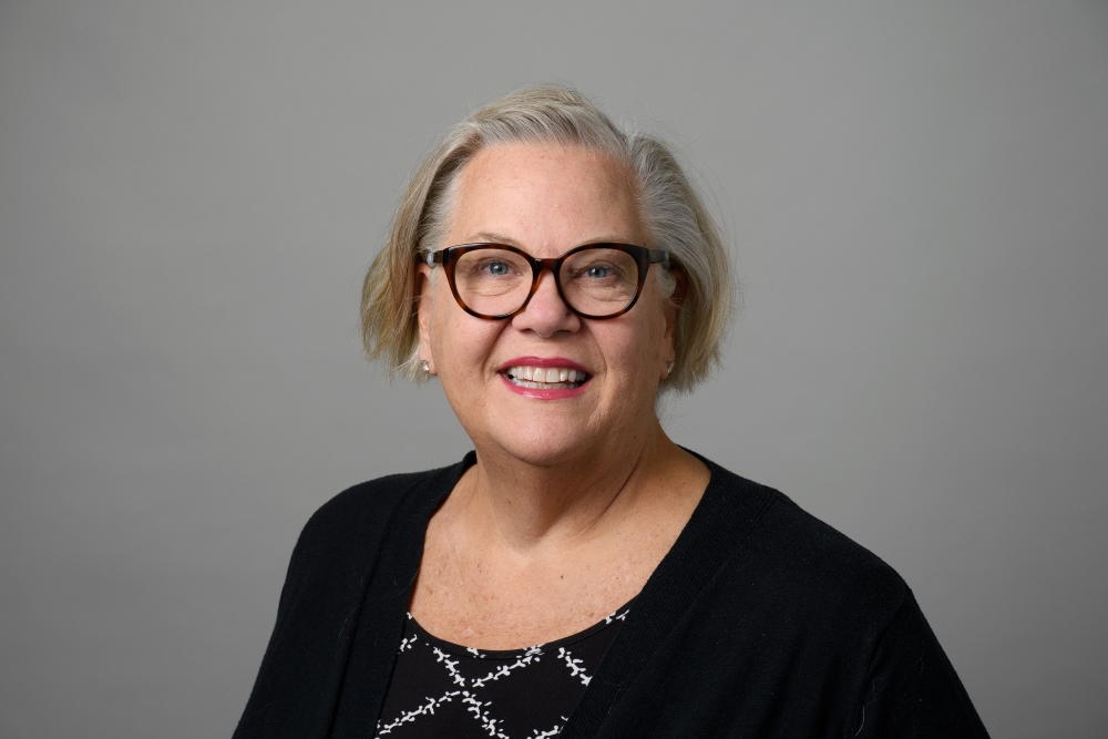 Portrait of Carol Ann Wetmore with glasses in front of a grey background